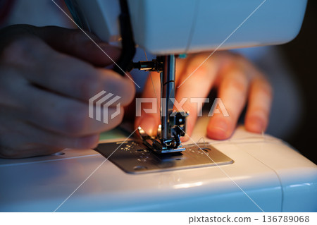 Sewing a delicate fabric piece in a cozy evening setting with focused hands at work 136789068