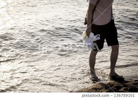A man walking on the sandy beach at the edge of the water A man walking on the sandy beach at the edge of the water 136789101