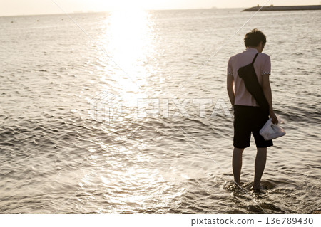 夕陽西下，一名男子漫步在沙灘上。 136789430