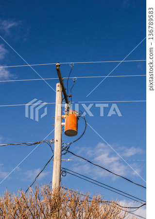 Wooden electricity pole with transformer and overhead power lines against clear blue sky in USA 136789583