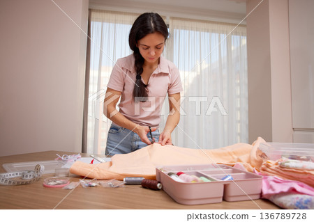 Woman focusing on cutting fabric using scissors for a diy craft project at home Woman focusing on cutting fabric using scissors for a diy craft project at home 136789728