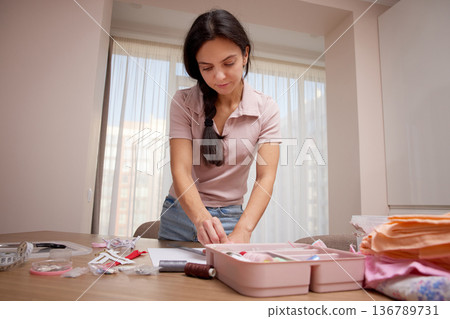 Woman focusing on drawing a fashion sketch at a table with sewing supplies Woman focusing on drawing a fashion sketch at a table with sewing supplies 136789731