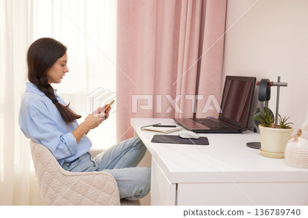 Woman playing with smartphone at desk, avoiding work on laptop in home office Woman playing with smartphone at desk, avoiding work on laptop in home office 136789740