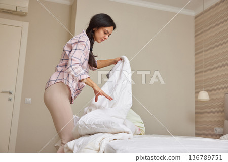 Woman making her bed, tidying up bedroom for a fresh start to the day 136789751