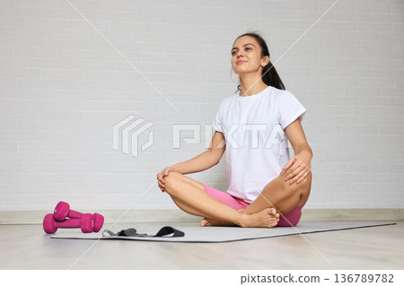 Woman sitting in lotus pose on a mat, meditating after exercise session at home Woman sitting in lotus pose on a mat, meditating after exercise session at home 136789782