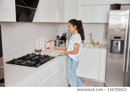 Young woman carrying a cutting board to prepare a meal in a modern kitchen Young woman carrying a cutting board to prepare a meal in a modern kitchen 136789822