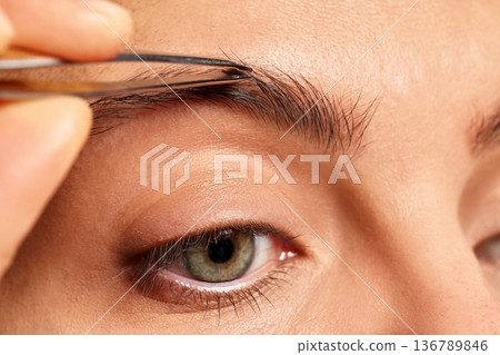 Woman tweezing her eyebrow, shaping and maintaining facial appearance Woman tweezing her eyebrow, shaping and maintaining facial appearance 136789846