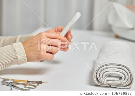 female hands filing nails with a nail file on a white table female hands filing nails with a nail file on a white table 136789852