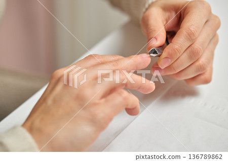 Person removing cuticles from nails using a nipper for grooming Person removing cuticles from nails using a nipper for grooming 136789862
