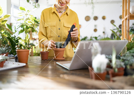 A woman is seen smiling as she plants a succulent in a pot, possibly following an online tutorial A woman is seen smiling as she plants a succulent in a pot, possibly following an online tutorial 136790126