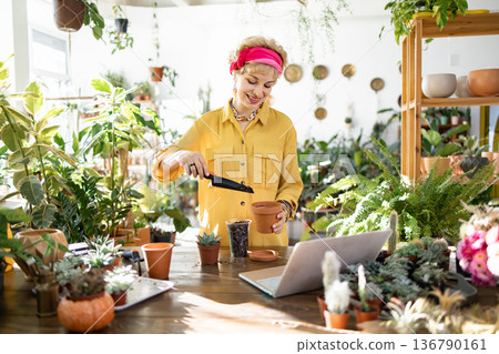 A woman in a yellow shirt is planting a succulent in a terracotta pot, enjoying the process 136790161