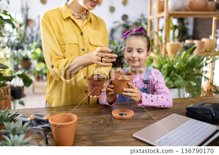 A woman and a young girl are repotting a succulent plant together, enjoying a fun activity A woman and a young girl are repotting a succulent plant together, enjoying a fun activity 136790170