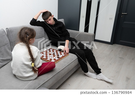 Engaging chess match between siblings in a modern living room on a cozy afternoon, showcasing concentration and strategic thinking Engaging chess match between siblings in a modern living room on a cozy afternoon, showcasing concentration and strategic thinking 136790984