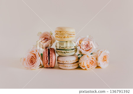 Tasty french macarons with tender rose flowers on a peach pastel background. Tasty french macarons with tender rose flowers on a peach pastel background. 136791392