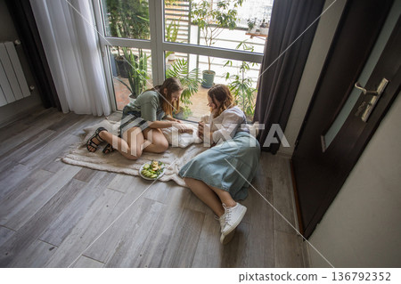 girl and women relax on a rug in a modern indoor space. They share snacks while sitting 136792352