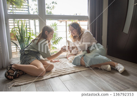 girl and women relax on a rug in a modern indoor space. They share snacks while sitting  136792353