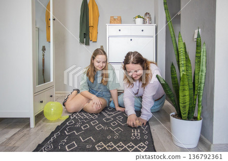 Two young women arrange a rug on the floor in a bright hallway with plants and furniture present 136792361