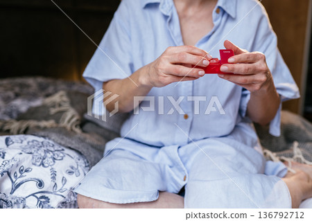 Close up of middle aged white woman in glasses holding capsule near lips before taking medication. Focused expression. Concept of treatment, depression support, mental health care. Close up of middle aged white woman in glasses holding capsule near lips before taking medication. Focused expression. Concept of treatment, depression support, mental health care. 136792712