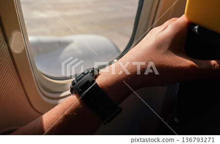 Sun shines on young man arm and plastic wristwatch near airplane window as he's waiting for takeoff 136793271
