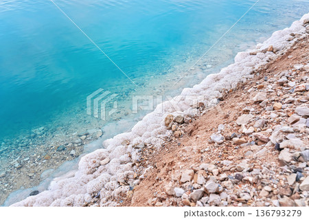 Sand covered with crystalline salt on shore of Dead Sea, turquoise blue water near - typical scenery at Ein Bokek beach, Israel 136793279