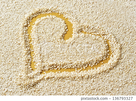 White sesame seeds on yellow desk, heart shape drawn with finger inside White sesame seeds on yellow desk, heart shape drawn with finger inside 136793327