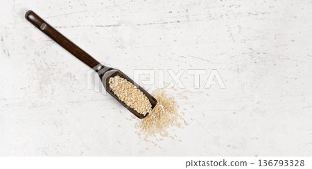 White sesame - Sesamum indicum - seeds in small wooden spoon on white stone like board, view from above, space for text right side White sesame - Sesamum indicum - seeds in small wooden spoon on white stone like board, view from above, space for text right side 136793328