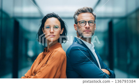 Confident business partners, a man and a woman, stand back-to-back in a modern office corridor. The concept of leadership, equality, and partnership. 136793384