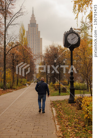 Strolling through a serene park with autumn colors and a clock tower in a cityscape backdrop 136793435