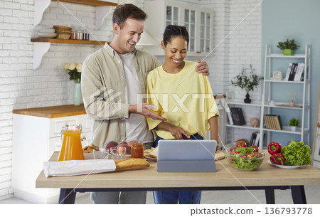 Couple cooking together at home kitchen, making salad with tablet recipe 136793778