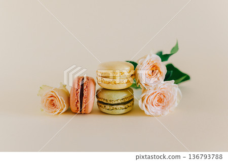 Tasty french macarons with tender rose flowers on a peach pastel background. Tasty french macarons with tender rose flowers on a peach pastel background. 136793788