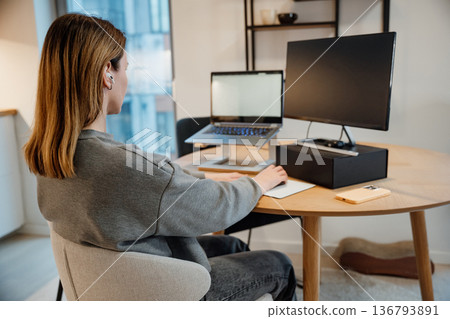 Woman working at home desk with laptop and monitor set up during daytime hours 136793891