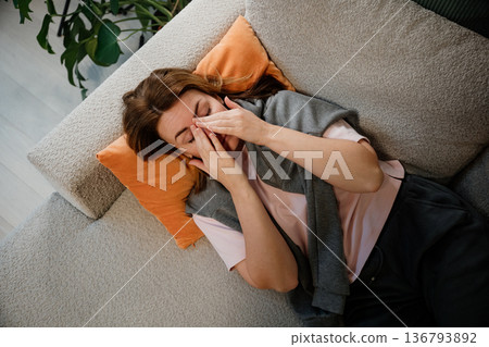 Women resting on couch with hands on face in living room during afternoon Women resting on couch with hands on face in living room during afternoon 136793892
