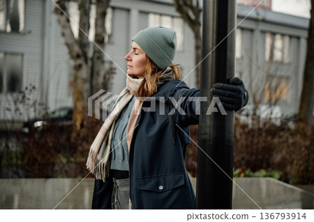 Woman enjoys cool weather while standing near a lamppost in an urban setting during autumn 136793914
