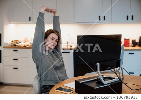 Woman stretching in home office while working on a computer during the day Woman stretching in home office while working on a computer during the day 136793915