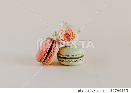 Tasty french macarons with tender rose flowers on a peach pastel background. Tasty french macarons with tender rose flowers on a peach pastel background. 136794185