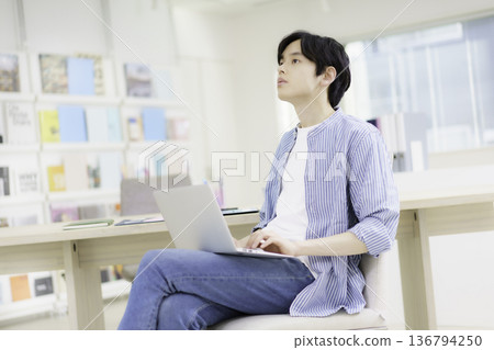 一位微笑的日本年輕男子正在辦公室操作筆記型電腦。 一位微笑的日本年輕男子正在辦公室操作筆記型電腦。 136794250