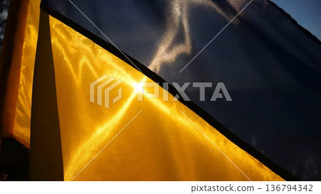 Blue-yellow symbol of Ukraine waving at wind against the background of sunlight. Ukrainian flag illuminated by sun fluttering at countryside. Concept of peace and support against russian aggression 136794342