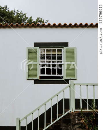 White house facade with a small window and green wooden shutters 136796913