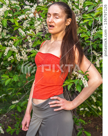 Young woman sneezes in the park against the background of a flowering tree. Allergy to pollen concept. Young woman sneezes in the park against the background of a flowering tree. Allergy to pollen concept. 136797126