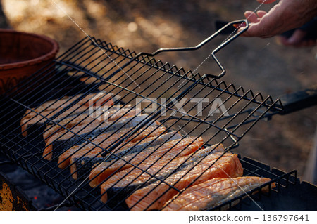 Grilling fresh salmon over an open flame in a serene outdoor setting during late afternoon 136797641