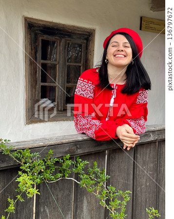 Smiling Woman in Traditional Red Outfit by Rustic Window 136797672
