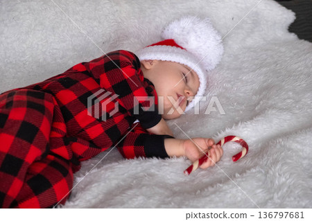 Sleeping baby in santa hat holding candy cane Sleeping baby in santa hat holding candy cane 136797681