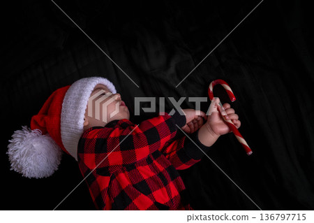 Sleeping baby in santa hat with candy cane on black Sleeping baby in santa hat with candy cane on black 136797715