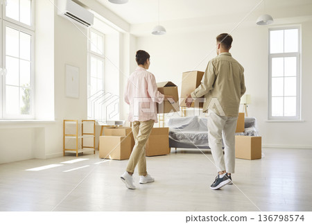 Couple carrying boxes while moving into bright new apartment with minimal decor 136798574