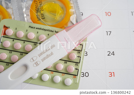 Pregnancy test with birth control pills and condom for female on calendar, ovulation day. Pregnancy test with birth control pills and condom for female on calendar, ovulation day. 136800242