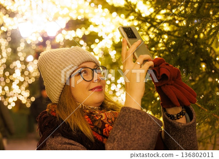 Delightful winter evening filled with lights as a woman captures the magic of twinkling decorations Delightful winter evening filled with lights as a woman captures the magic of twinkling decorations 136802011