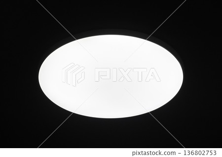 Bright circular ceiling light fixture casting an even white glow against a black ceiling Bright circular ceiling light fixture casting an even white glow against a black ceiling 136802753