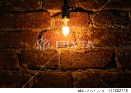 A glowing vintage light bulb hangs against a rustic red brick wall A glowing vintage light bulb hangs against a rustic red brick wall 136802758