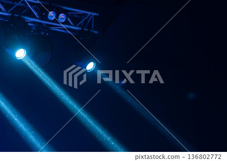 Blue spotlights cast dramatic beams through haze over a concert stage truss 136802772