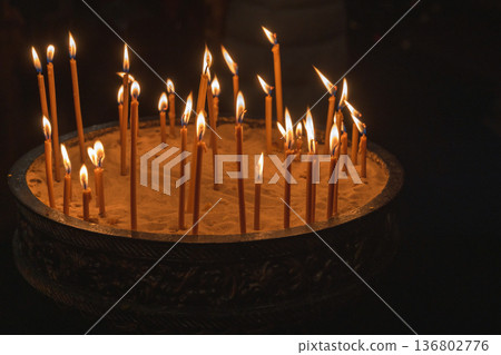 Sacred dark church scene featuring a round sand tray with lit prayer candles 136802776